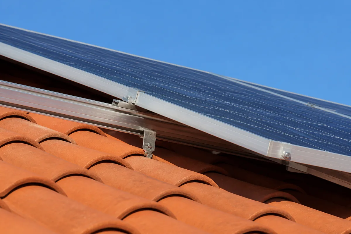 Panneaux photovoltaiques en surimposition sur une toiture en tuiles rouges, pente marquee, ciel degage de fin de matinee