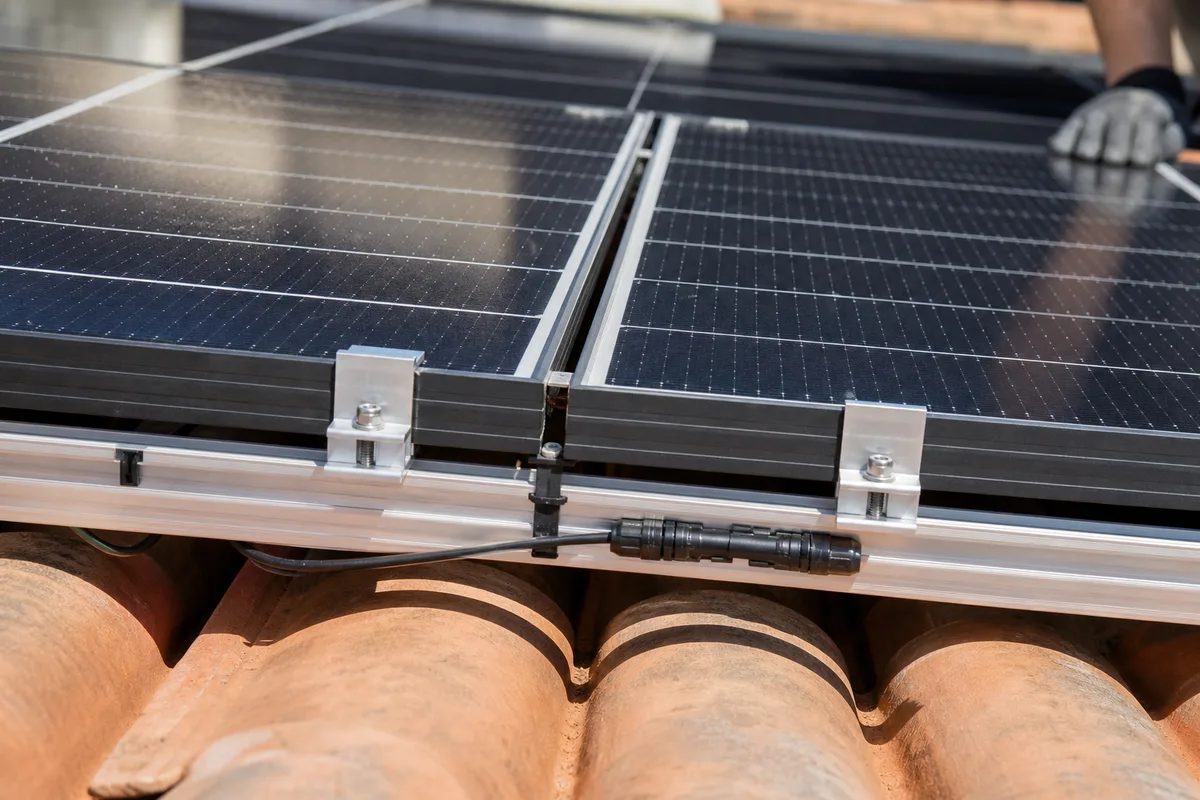 Panneaux photovoltaïques en surimposition sur une toiture en tuiles, rails de fixation visibles sous lumière franche